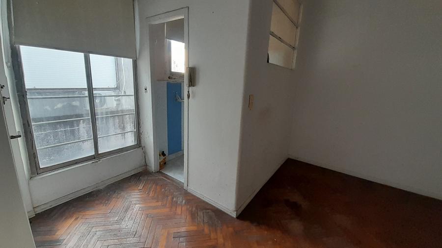 Living comedor del dpto. oficina de Tucumán al 1700: piso de parquet en espiga, un ventanal a la izquierda y paredes blancas con desgaste